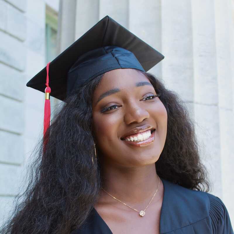 Aisha smiles, wearing a black graduation cap