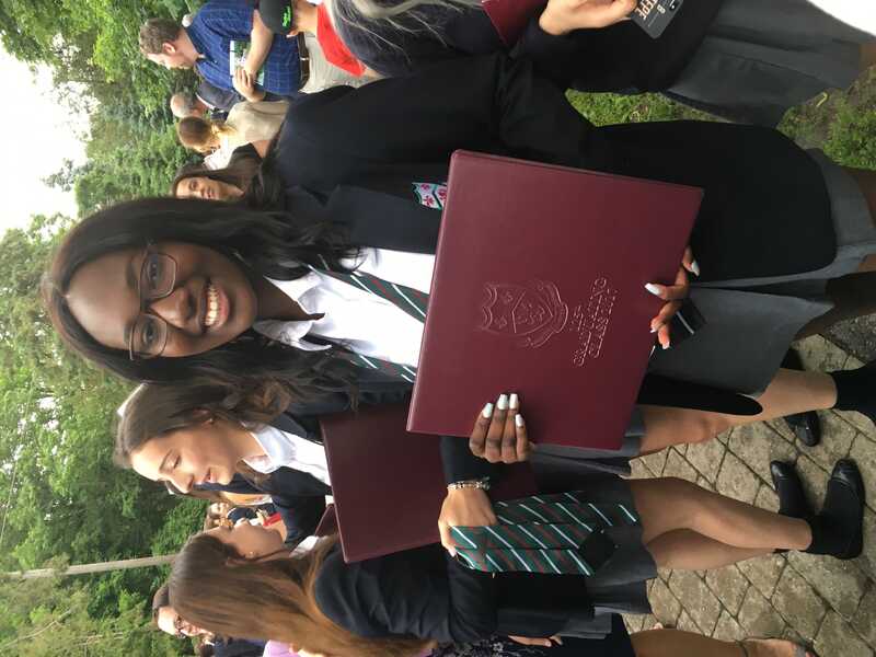 Aisha in a school uniform, holding her graduation certificate that says “class of 2017”