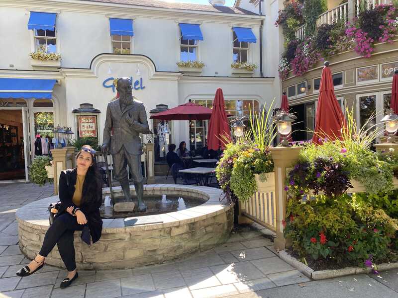  A woman sits on the edge of a fountain with a statue behind her.