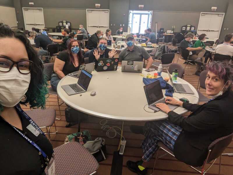 A photo showing participants at Contribution Day at DrupalCon Pittsburgh sitting around a table with their laptops 