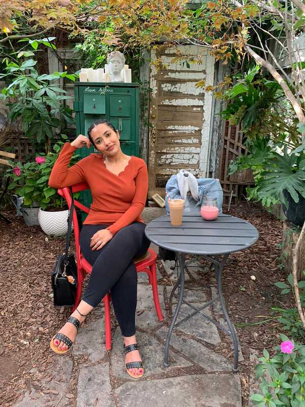 Woman sitting at table with two drinks surrounded by vegetation