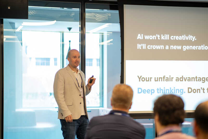 Shawn presenting, standing in front of a screen that says AI won't kill creativity.