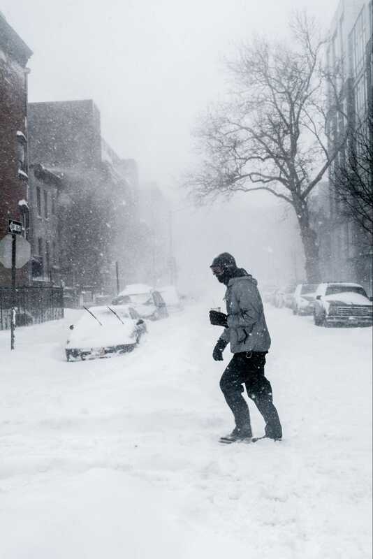 ​​​​​​​Alt text: A person walks through the snowy streets with a drink in hand.