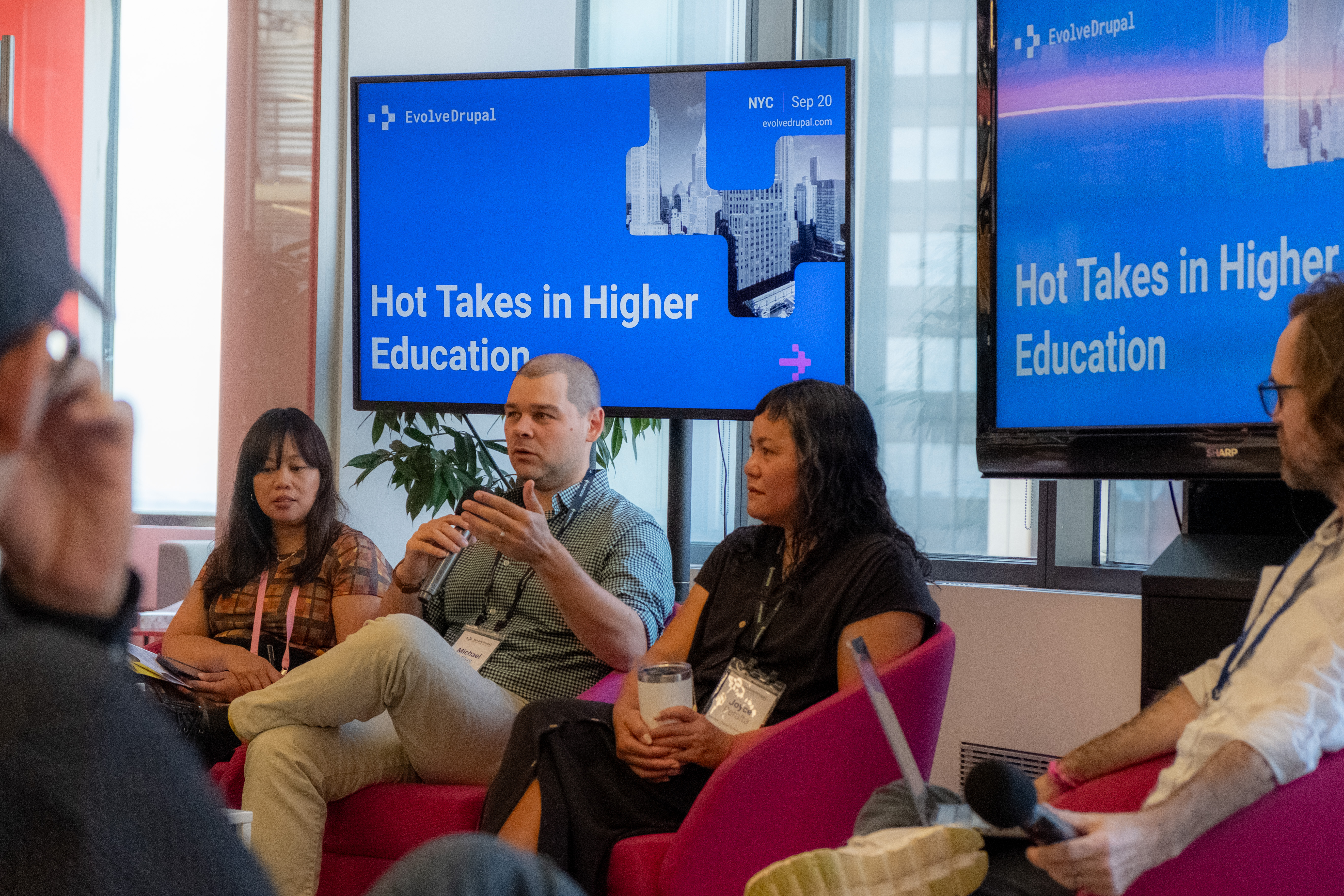 A panel of speakers sitting in pink chairs in front of an audience, under blue screens that announce the panel name