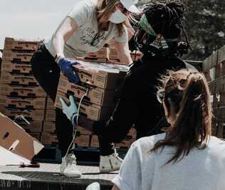 Two women and man unloading a pick up truck with food supplies for charity