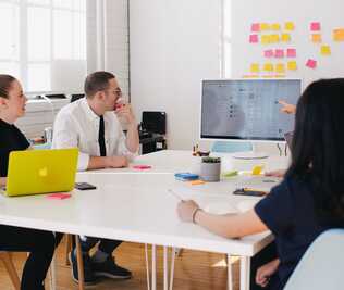 3 people in a meeting room looking a computer screen on a table.