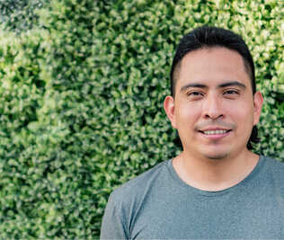 A portrait of a person facing the camera and smiling against some bright green bushes.