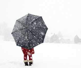 Person standing in the snow with a black umbrella and red pants.
