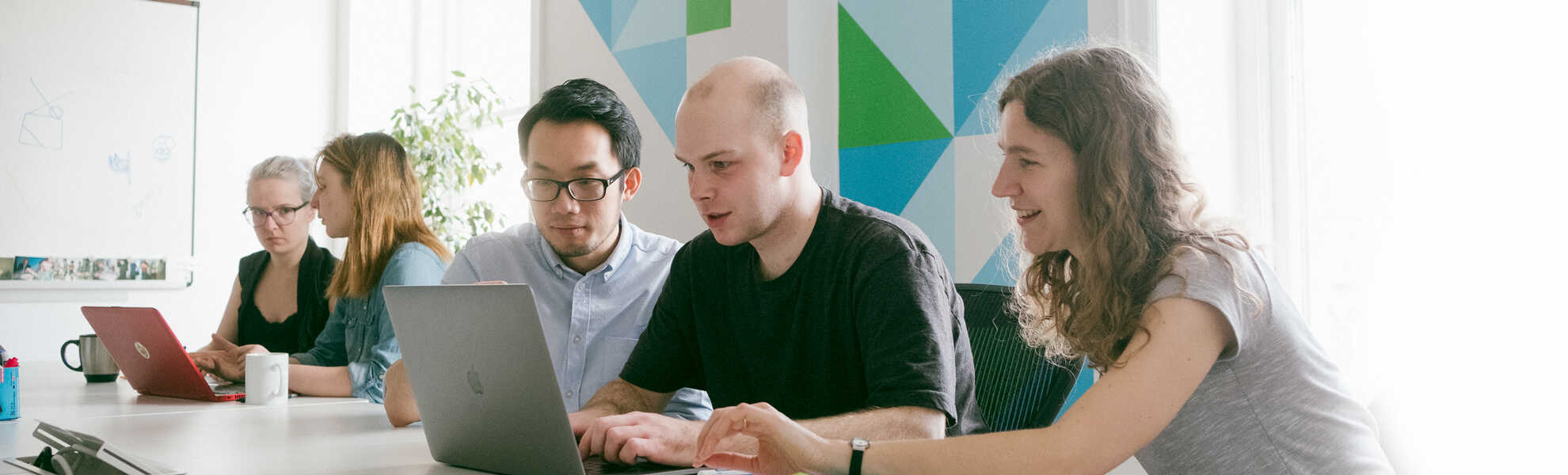 five persons working together at a table around a computer
