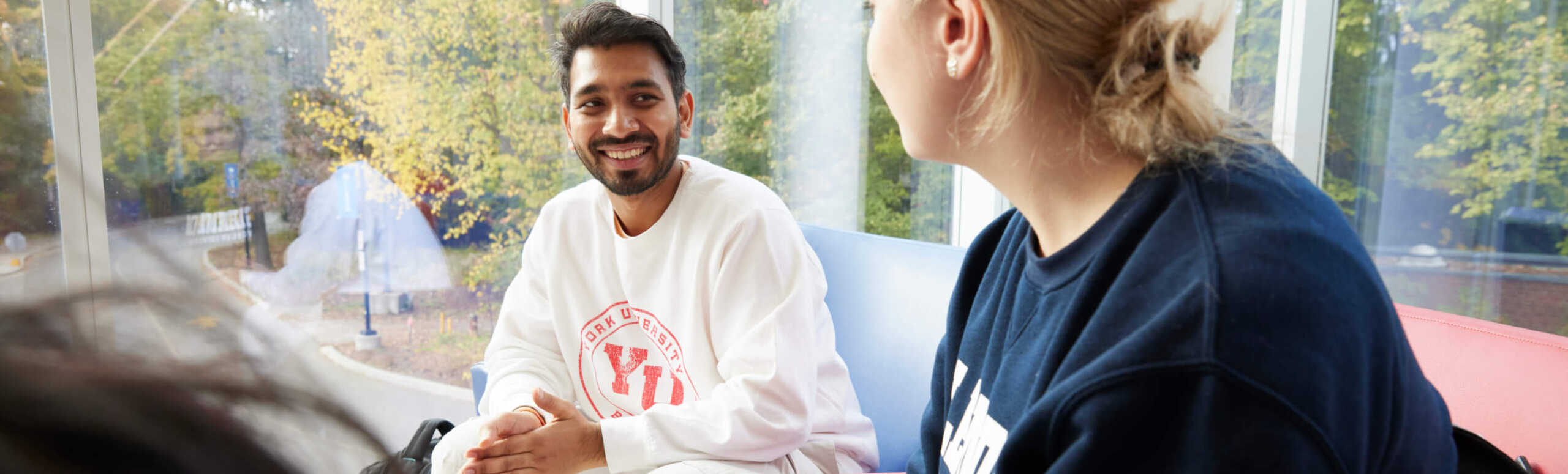 A man and a woman smile at each other while sitting in front of a window.