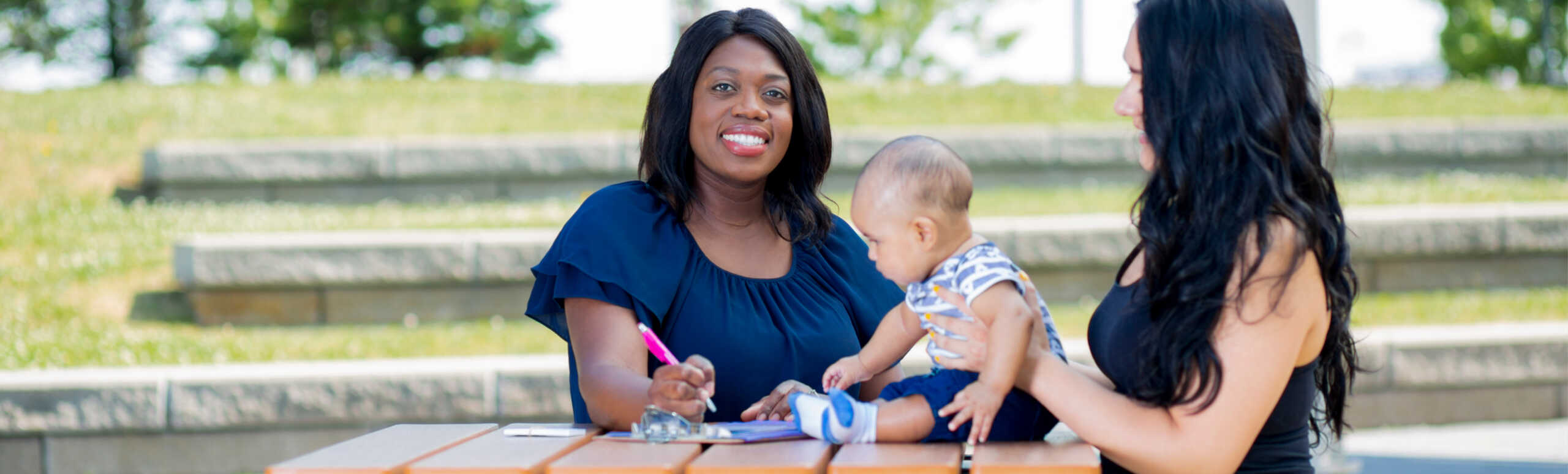 Two women and a baby sitting at a table outside