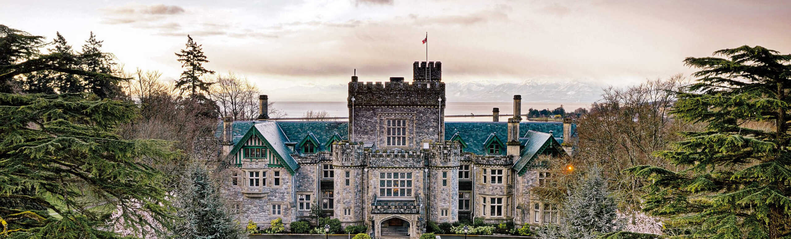 The Royal Roads University main building surrounded by trees with the mountains in the background