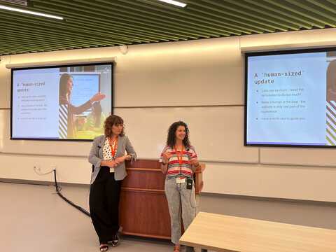 Two people presenting at a conference in front of screens on the left and right