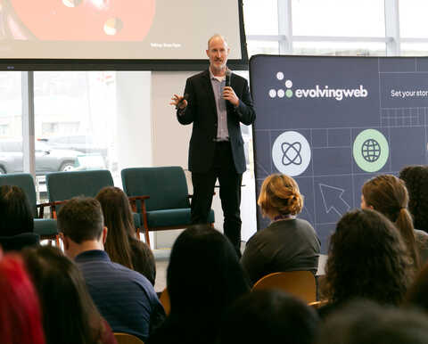 Brian Piper presenting on a stage with the audience visible in the foreground.