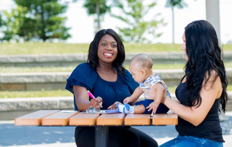 Two women and a baby sitting at a table outside