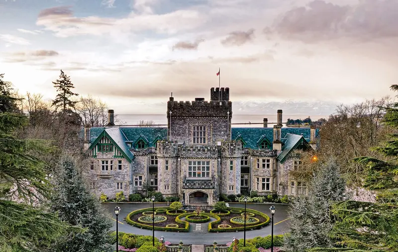 The Royal Roads University main building surrounded by trees with the mountains in the background
