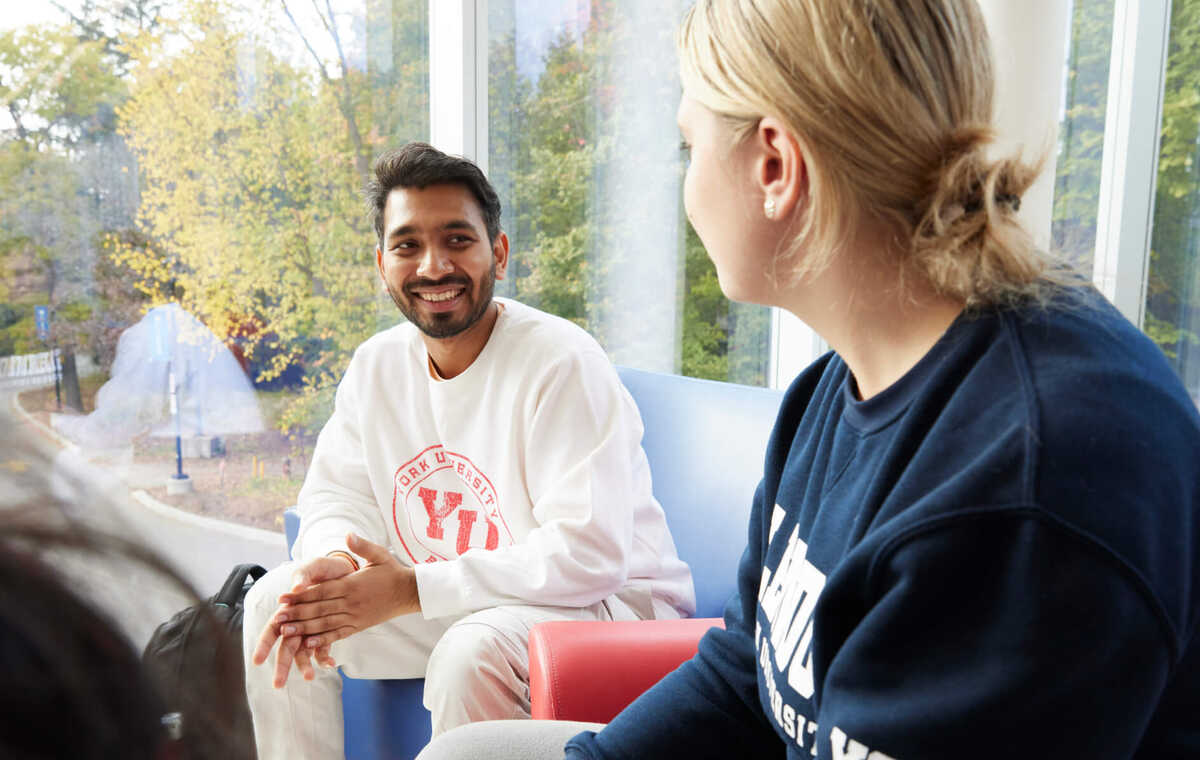 A man and a woman smile at each other while sitting in front of a window.