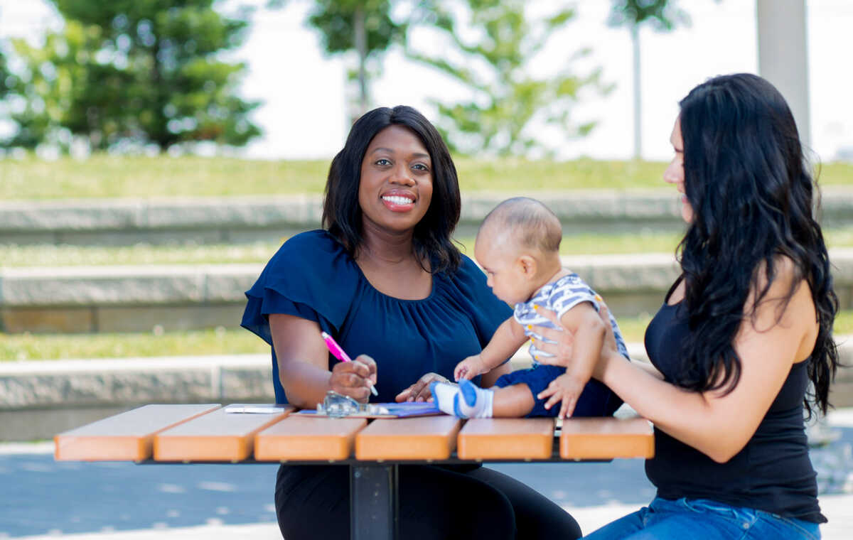 Two women and a baby sitting at a table outside