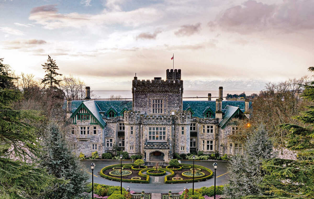 The Royal Roads University main building surrounded by trees with the mountains in the background